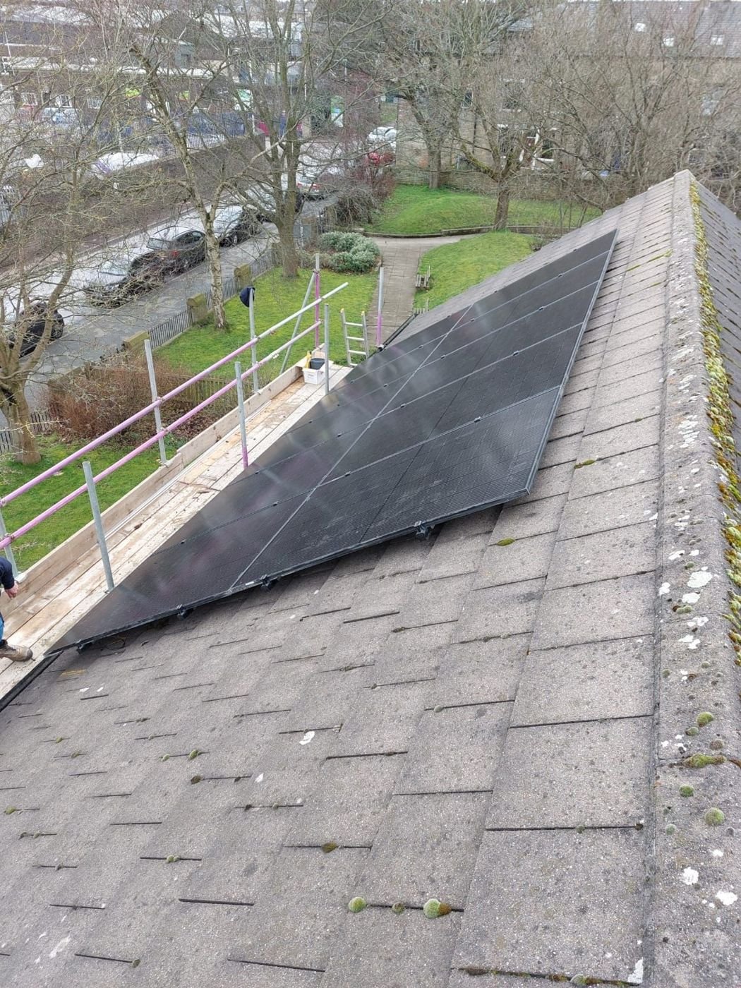 All-black solar panels on a grey concrete-tile roof, with scaffold edge protection