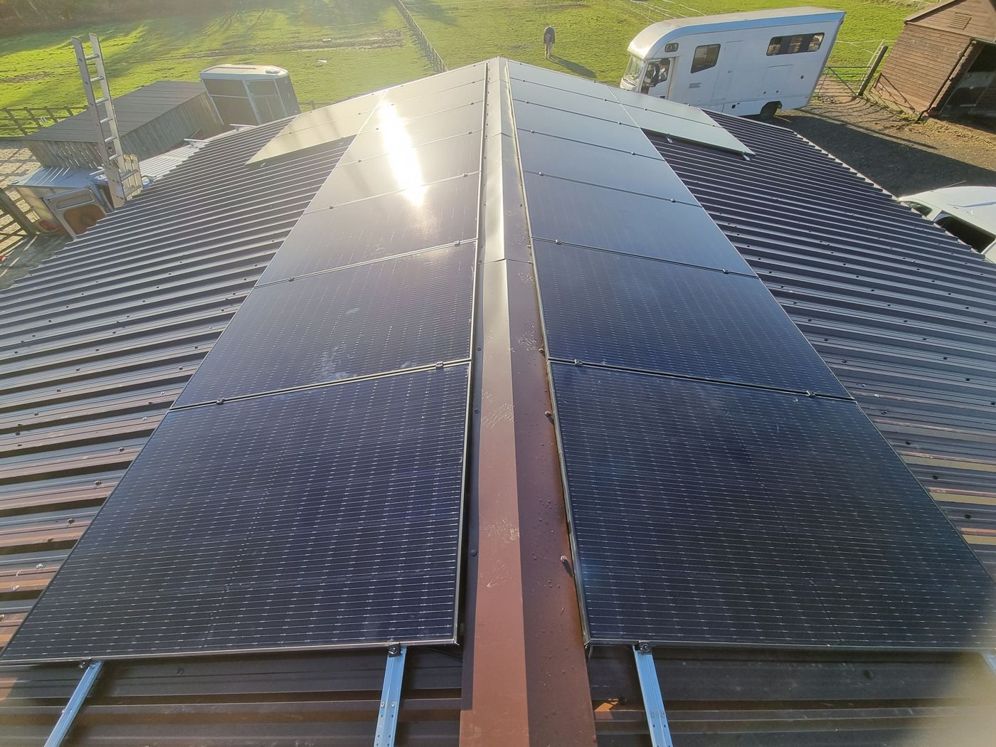 All-black solar panels on mounting rails on both sides of the ridge of a corrugated metal barn roof