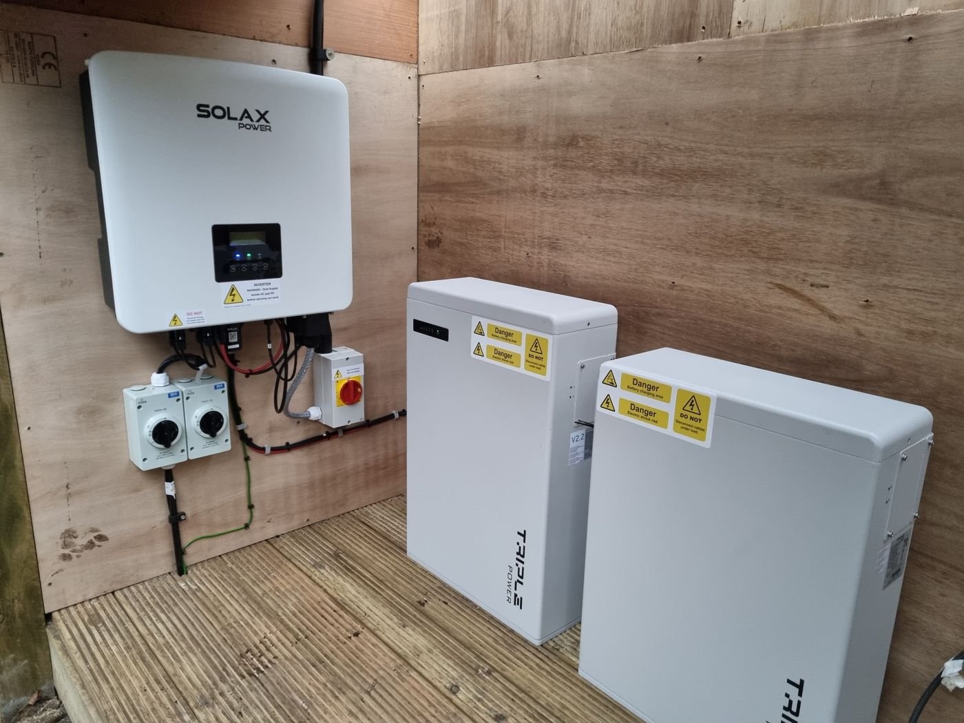 A SolaX hybrid inverter with two SolaX Triple Power batteries and isolator switches, fitted in a plywood enclosure